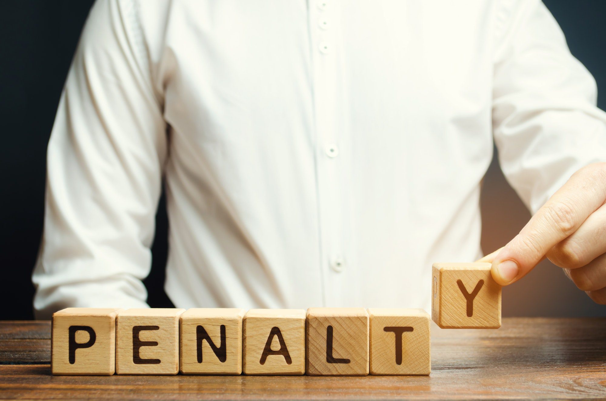 A man puts a wooden blocks with the word Penalty spelled out for his Part D late enrollment.