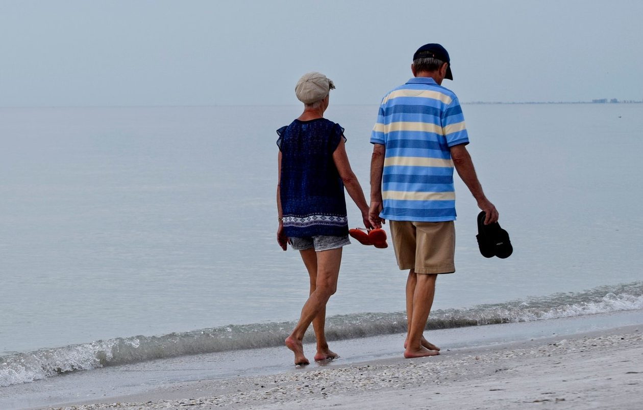 Senior couple walking along a Florida beach discussing their medicare options.