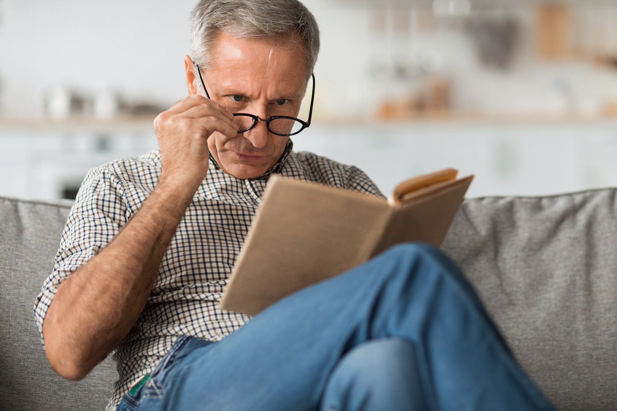 Senior man with poor eye sight trying to read a book as he thinks over if his medicare covers visions care.