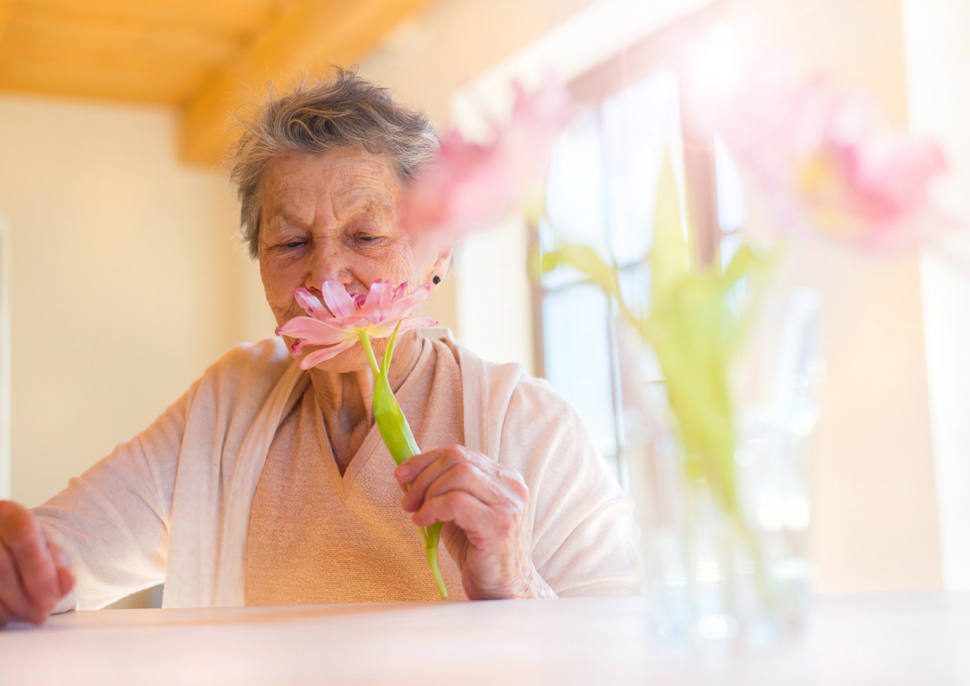 Senior woman enjoying the smell of flowers as discusses starting medicare with friends.